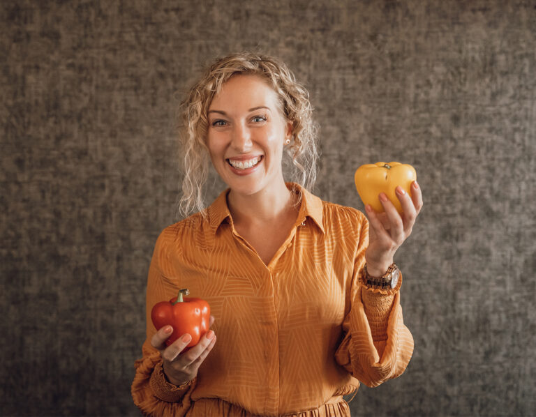 Glimlachende blonde vrouw houd gezonde voeding vast in haar handen het zijn twee paprika's.