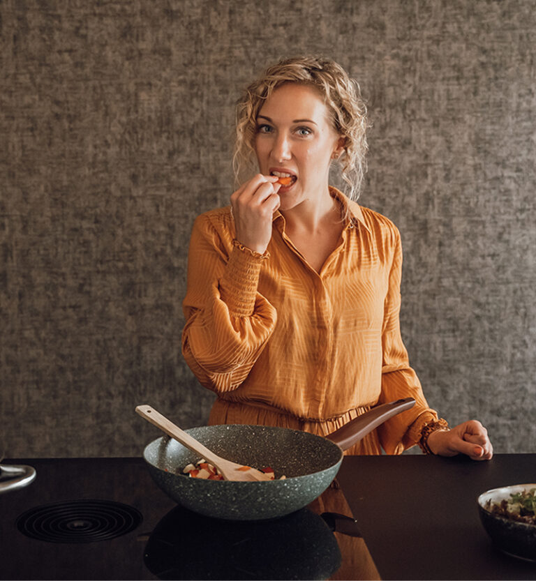 Blonde vrouw met krullen eet een stuk gezond voedsel uit een wokpan.