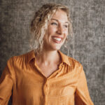 Geertje van Puur voeding bij Geertje in een gele jurk kijkt opzij en lacht.