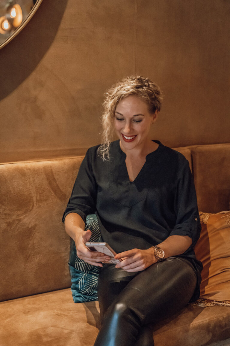 Blonde vrouw met krullen met glimlach en telefoon in de hand.