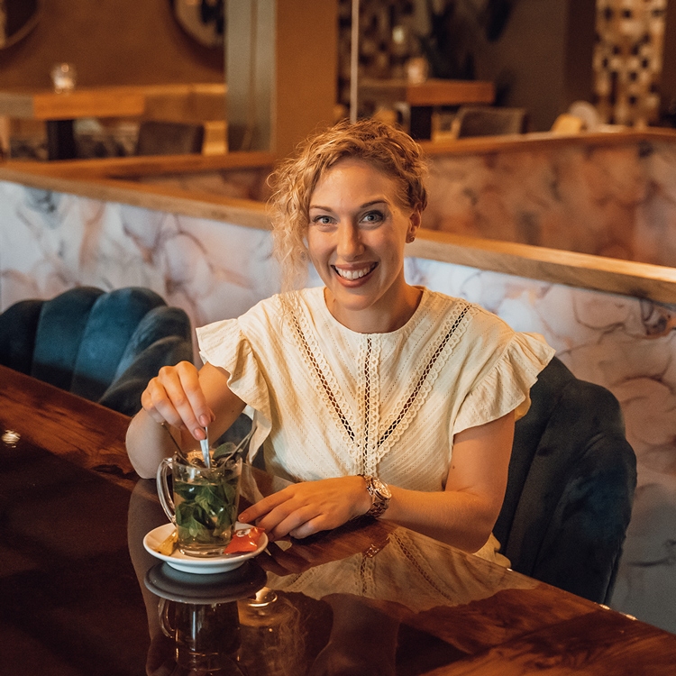 Vrouw glimlachend met blonde krullen drinkt een kruidenthee.