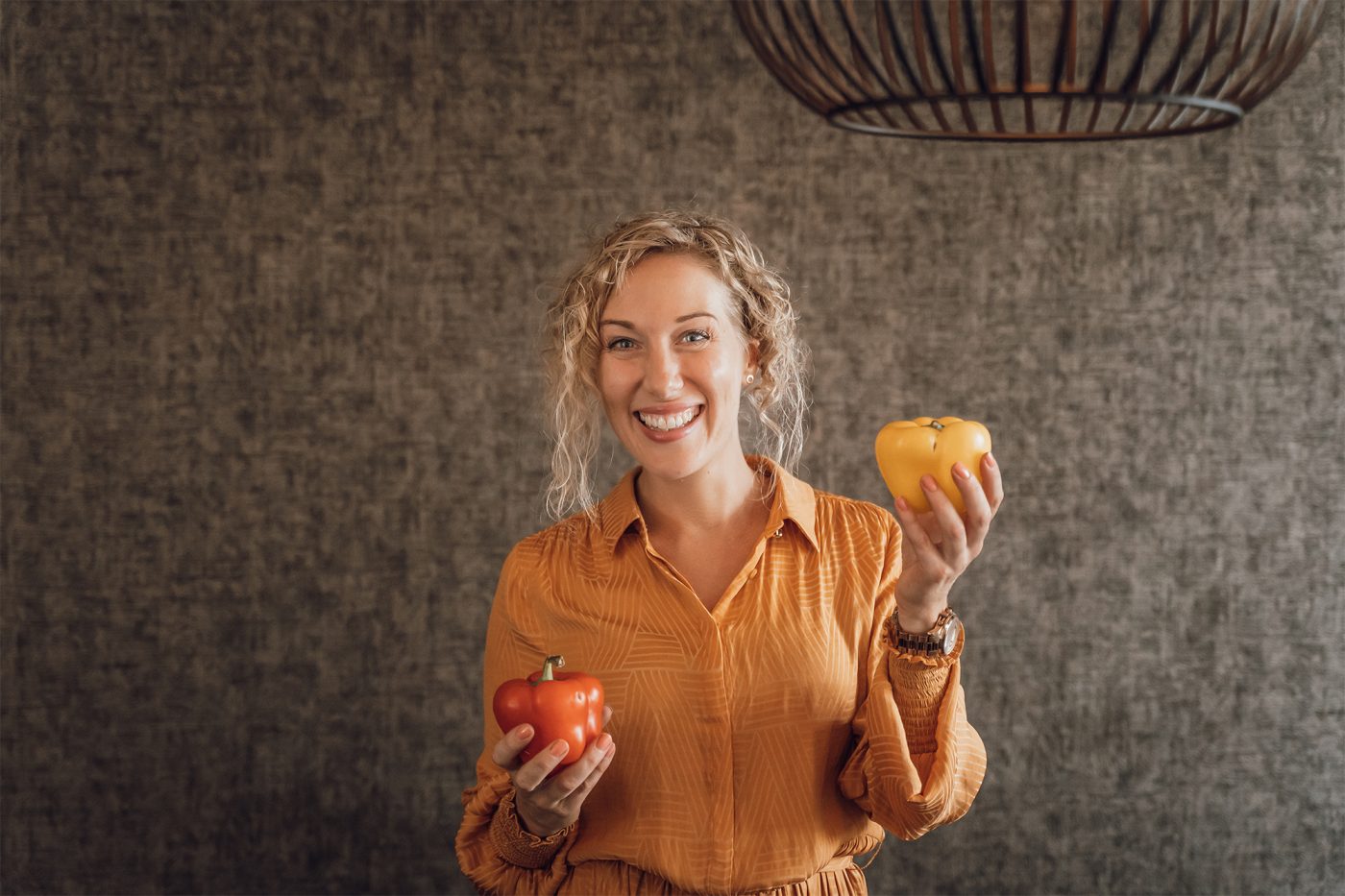 Glimlachende blonde vrouw houd gezonde voeding vast in haar handen. Het zijn twee paprika's.